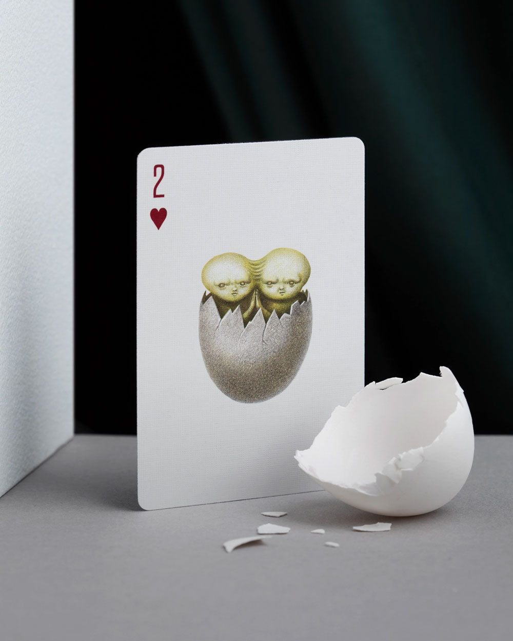 2 of hearts playing card with two-headed figure emerging from a cracked egg