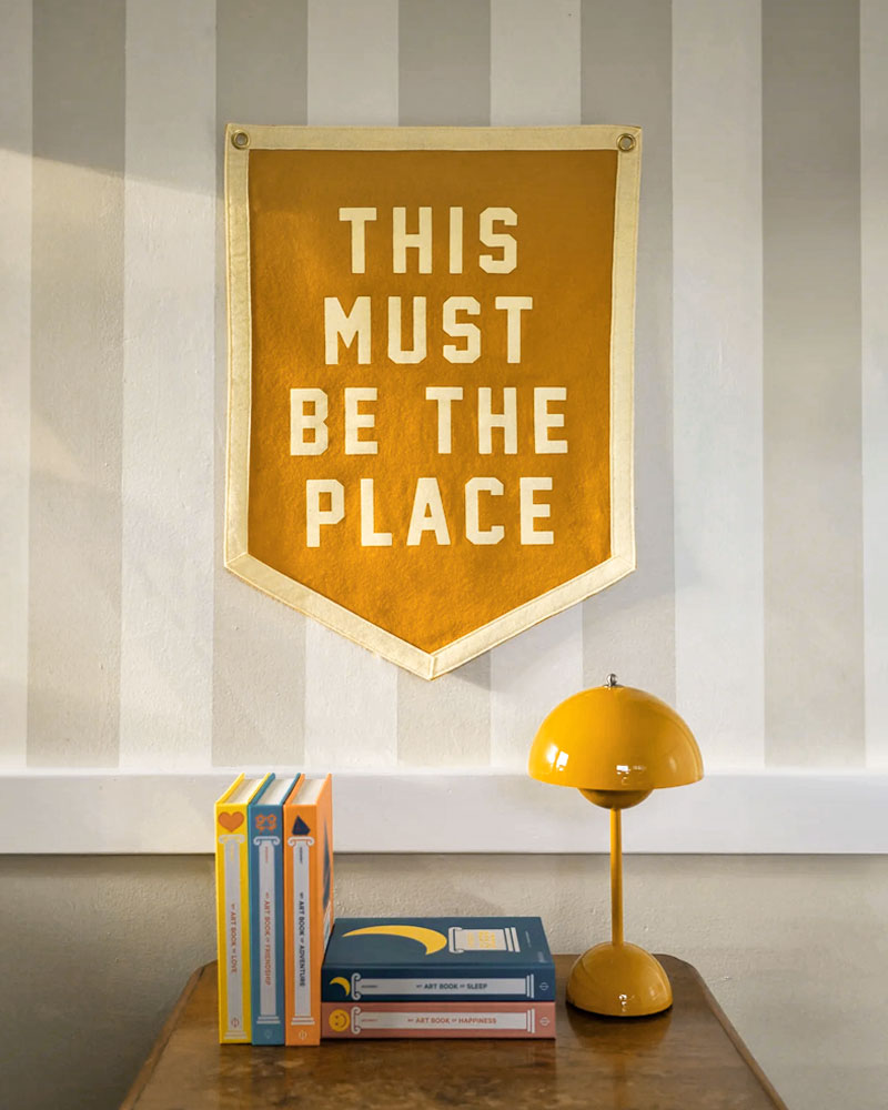 Orange felt flag banner with white text 'THIS MUST BE THE PLACE' and metal grommets