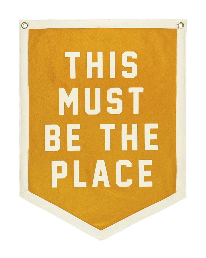 Orange felt flag banner with white stacked text 'THIS MUST BE THE PLACE' and grommets