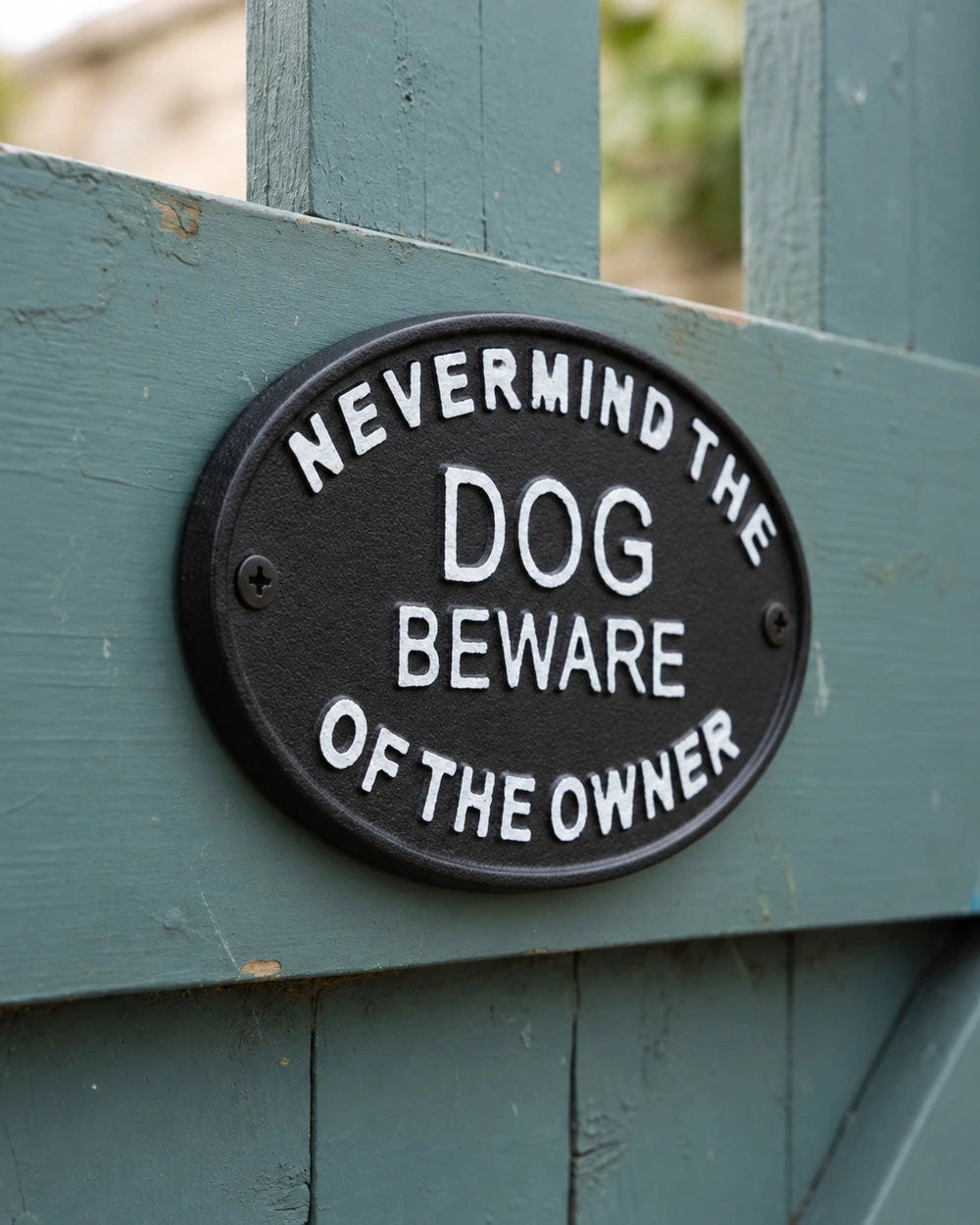 Close-up round black sign reading "DOG BEWARE OF THE OWNER"