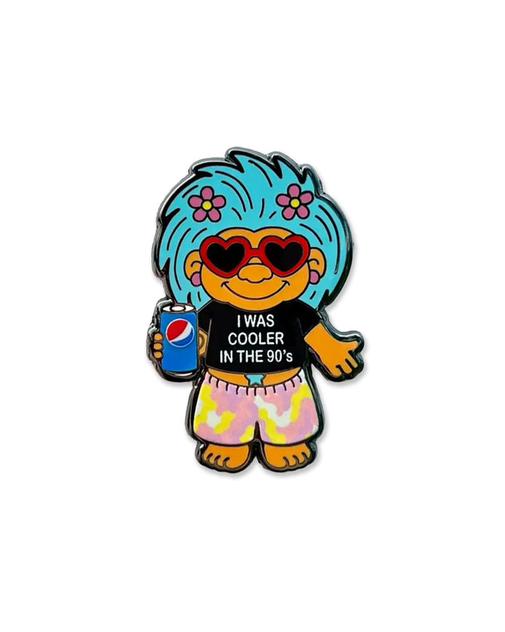 Cartoon troll enamel pin with blue hair, red heart glasses, holding a drink; says 90's