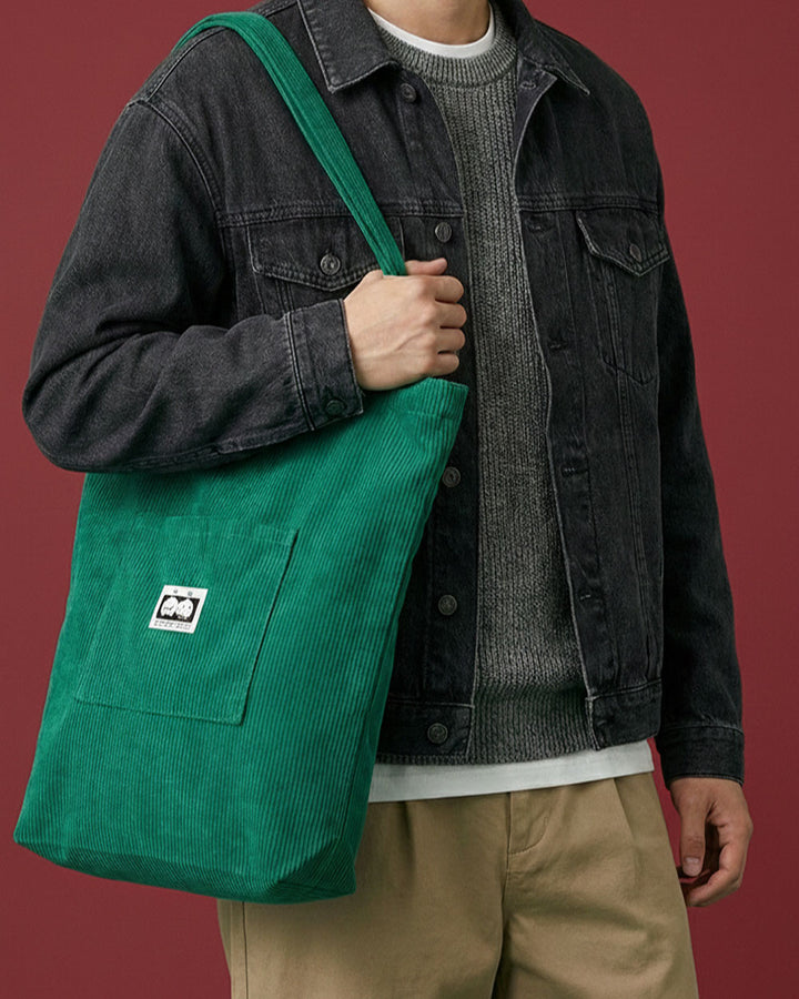 Green corduroy tote bag carried over shoulder with front pocket and logo label