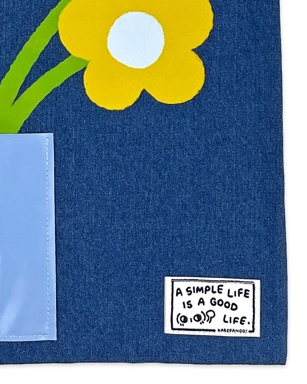Denim tote close-up with white front pocket and floral patch with quote label