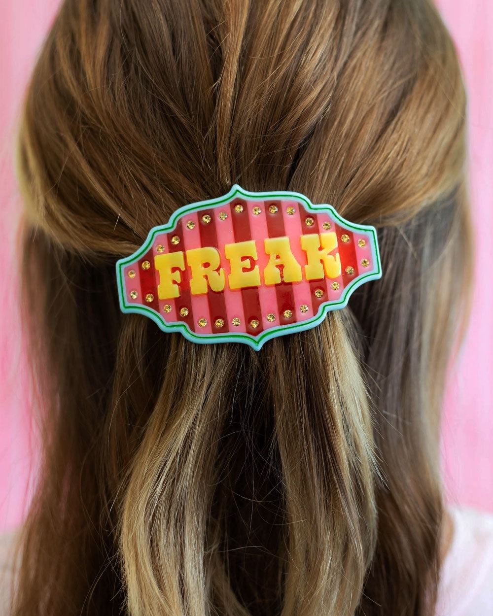 Freak show hair clip on blonde hair, red striped badge with green outline
