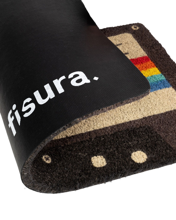 Cassette doormat corner with white "f1sura-" text on black fabric and tufted edge
