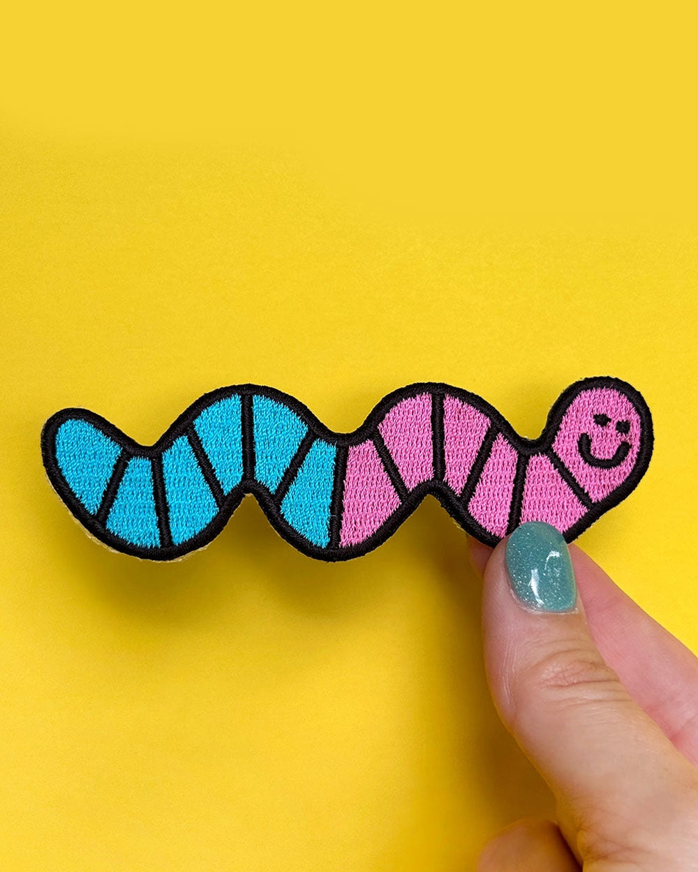 Gummy worm patch with blue/pink stripes and smiling face, held by fingertip