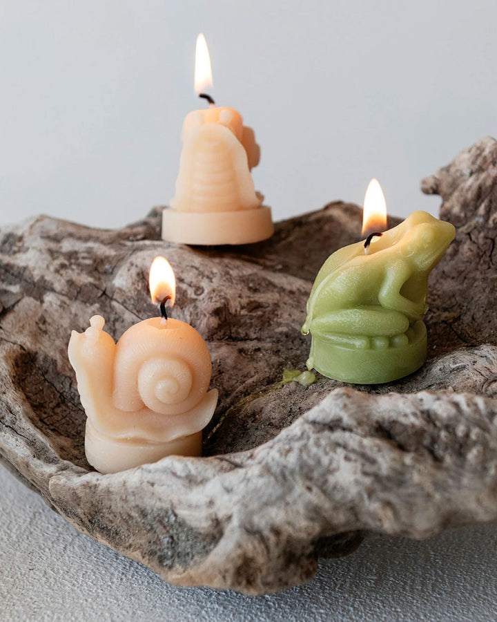 Snail-shaped tea light candles in metal cups, lit, cream and light green