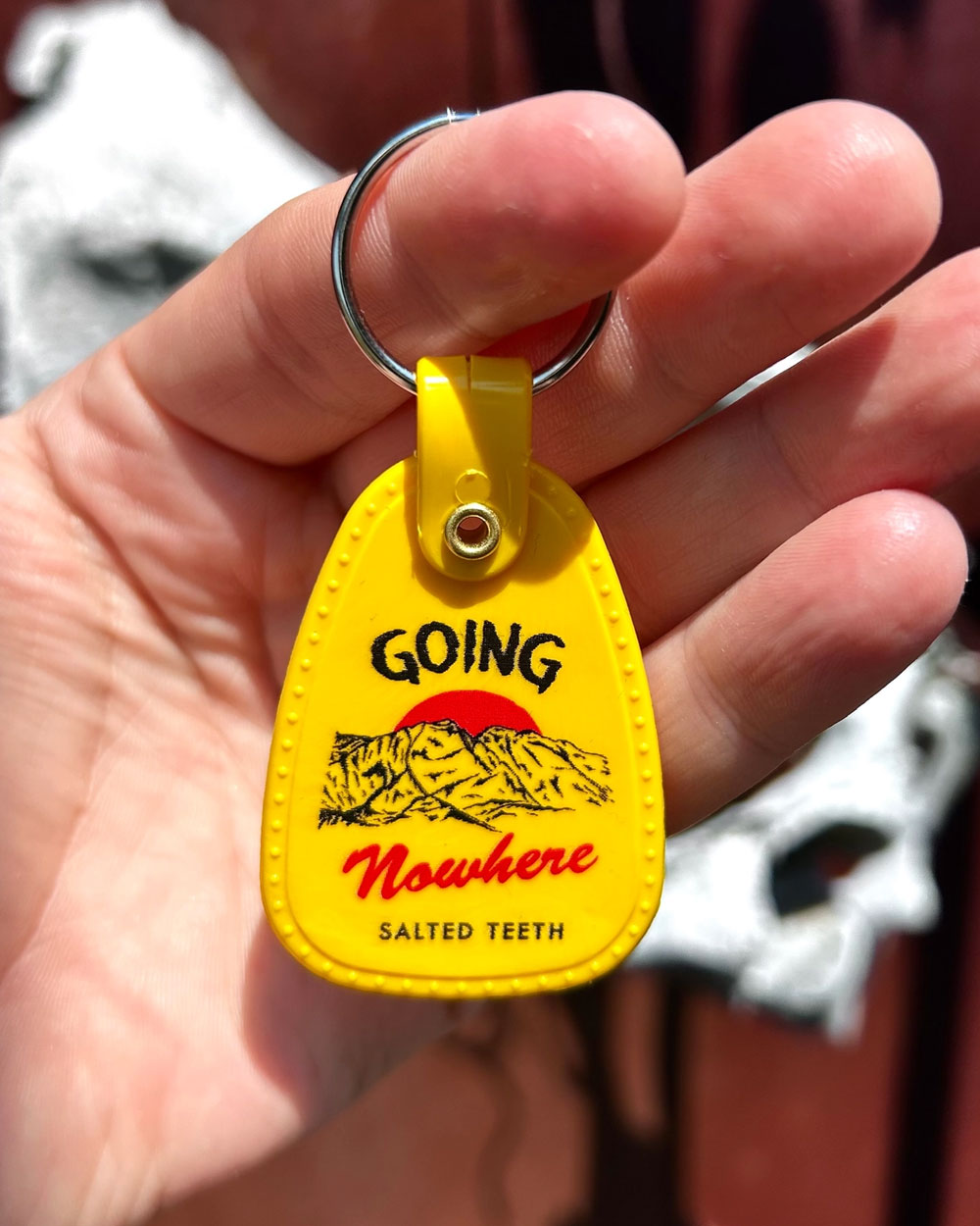 Yellow teardrop keychain with metal ring, 'GOING Nowhere' print; held in hand