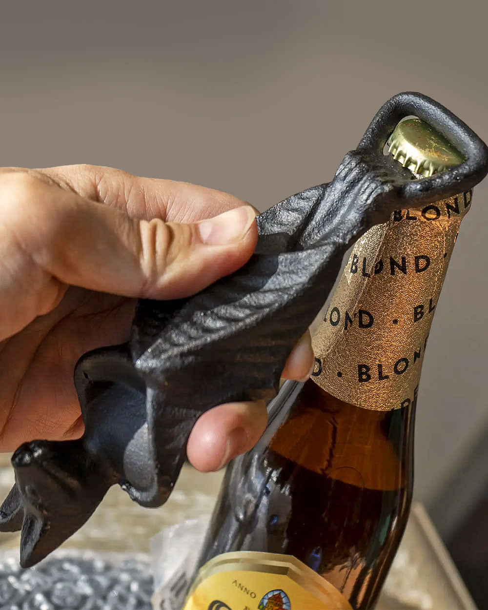 Dark metal cat bottle opener in hand gripping a bottle cap