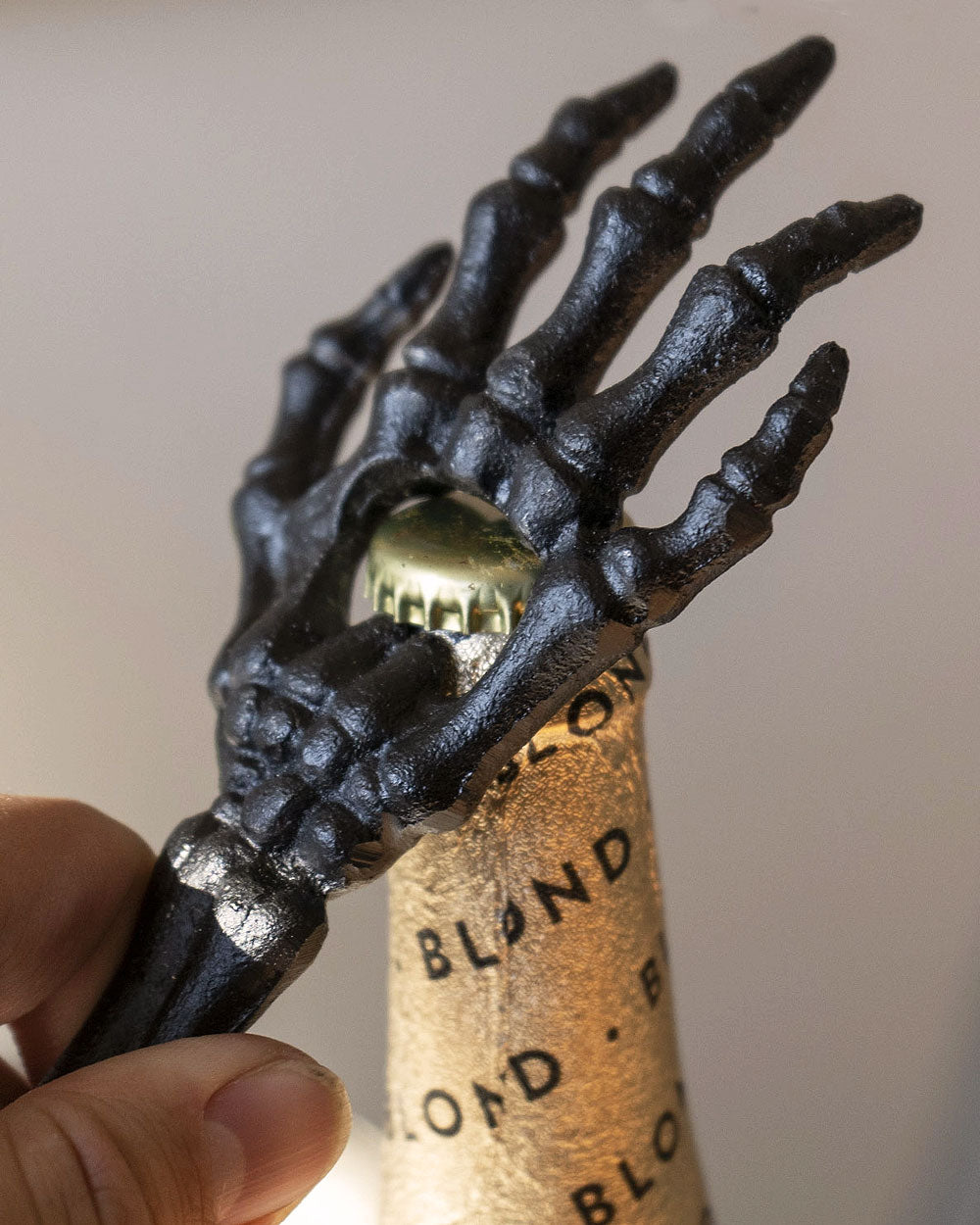 Skeleton hand bottle opener holding a gold bottle cap, spiky finger details