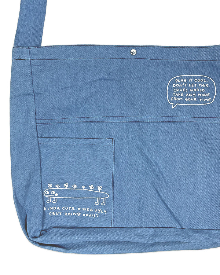 Blue denim tote bag with front panel pocket and stitched graphic detail