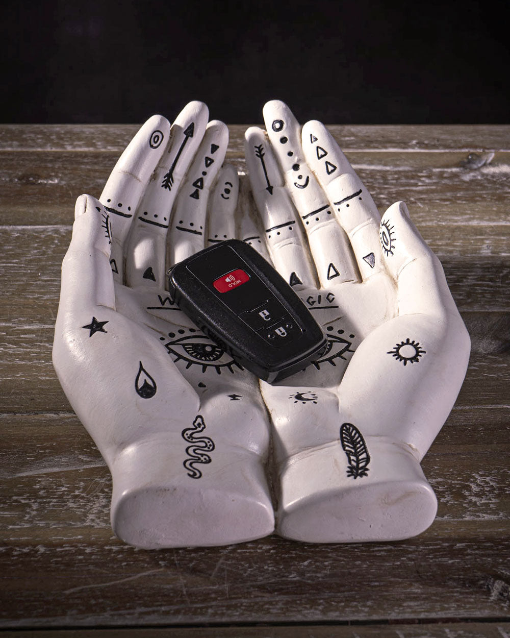 White resin hand holder with mystical icons and a black device in the palm