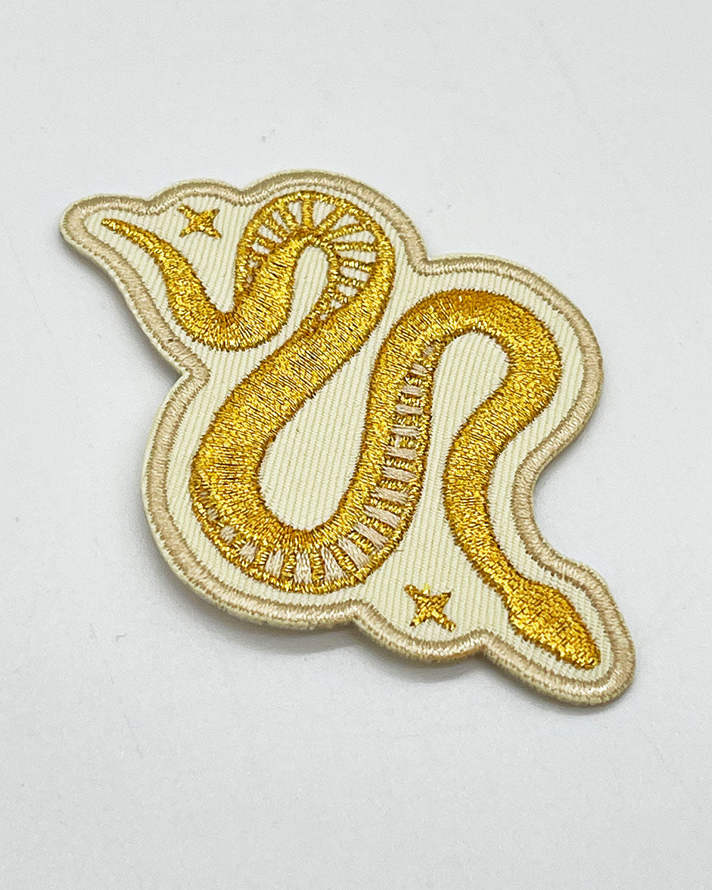 Close-up of gold and cream snake patch embroidery with outlined swirls and stars