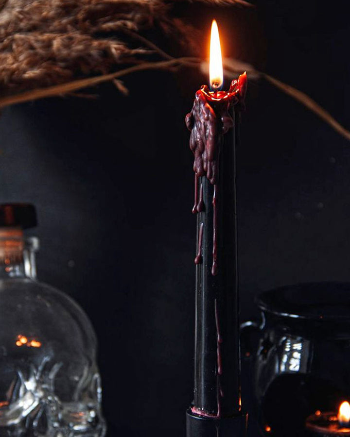 Black taper candle with red drip details, burning flame