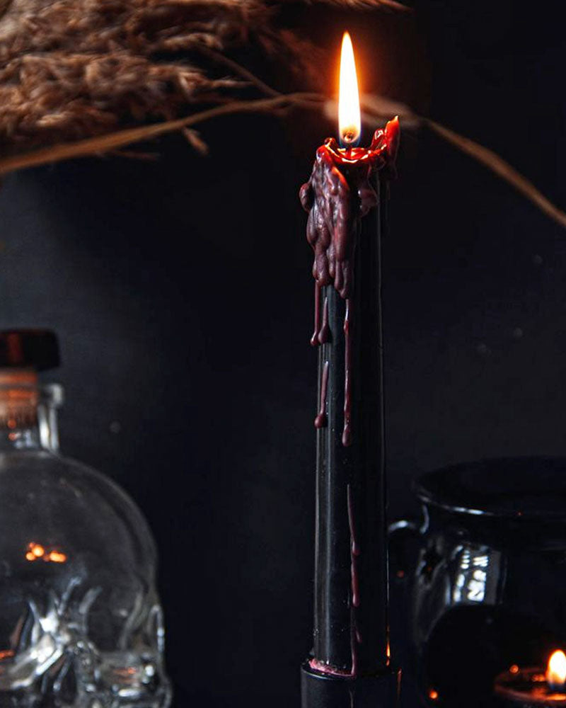 Black taper candle with red drip details, burning flame