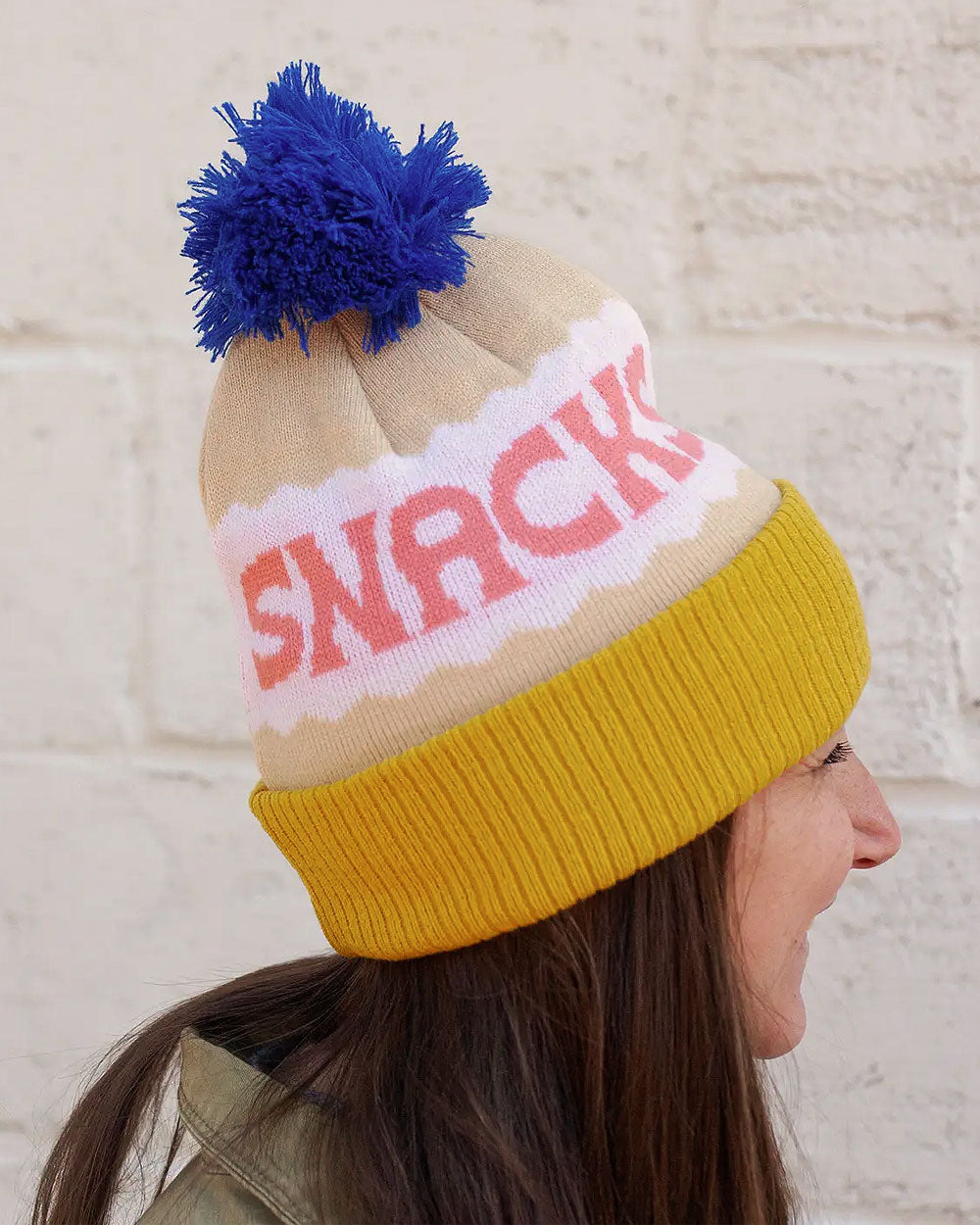 Pom beanie on model: blue pom, beige knit with pink logo text, mustard cuff