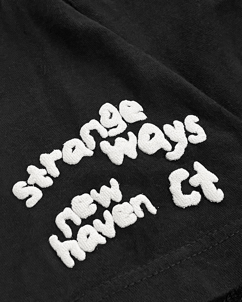 Black unisex T-shirt detail: white raised text print on the front