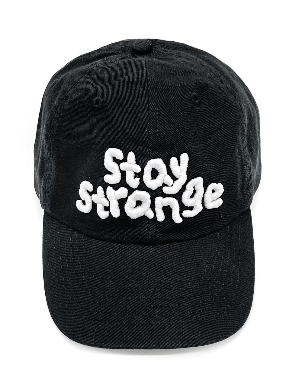 Black dad hat with white embroidered “Stay Strange” text on front