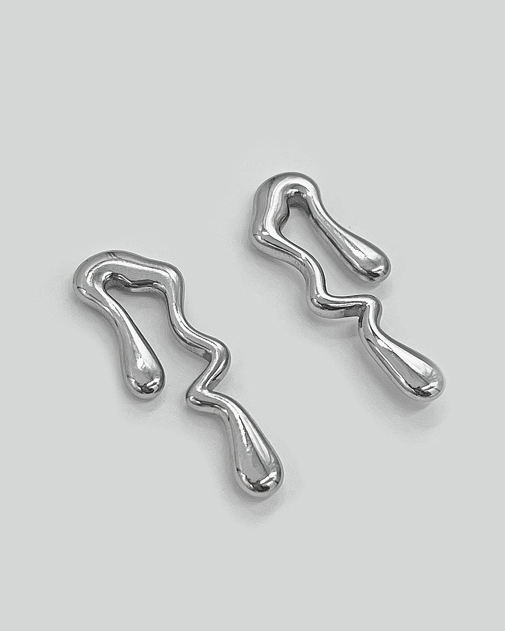 Pair of silver-tone abstract wavy drop earrings, one angled, polished finish