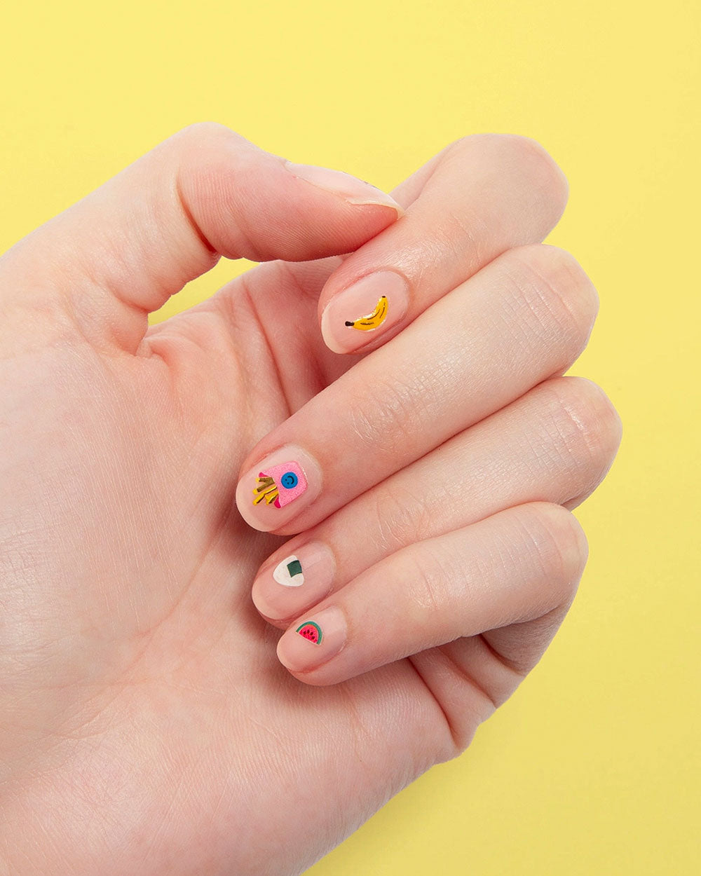 Hand with short nails featuring colorful food nail art stickers.